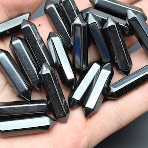 May include: A collection of black obsidian points, also known as arrowheads, are displayed on a hand. The points are smooth and polished, with a sharp tip and a flat base.