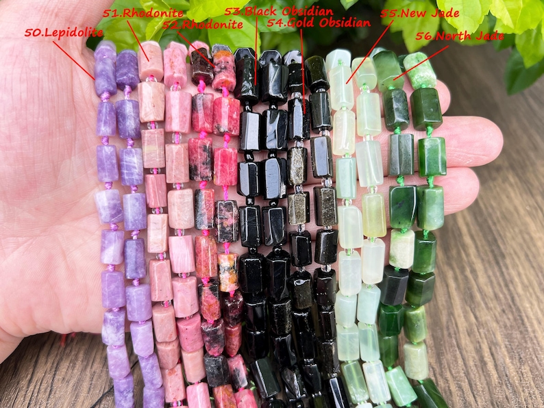 May include: Strands of gemstone beads in various colors, including purple lepidolite, pink rhodonite, black obsidian, and green jade. Each bead is a rectangular shape, strung together with pink thread.