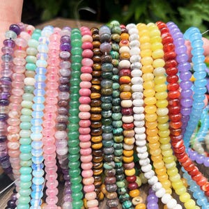 Peut inclure: Une collection de multiples brins de perles en pierre gemme rondes et lisses dans une variété de couleurs incluant violet, bleu clair, rose, vert, marron, blanc, jaune, orange et rouge, enfilées sur des fils de filament transparents.