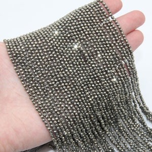 Puede incluir: Una hebra de cuentas de pirita de color plateado, cada cuenta está facetada y tiene una forma ligeramente irregular. Las cuentas están enhebradas en un hilo transparente y tienen aproximadamente 2 mm de diámetro.