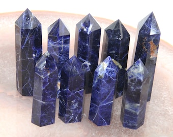 May include: A collection of eight blue and white sodalite crystal points. The points are arranged in a semi-circle on a pink surface.