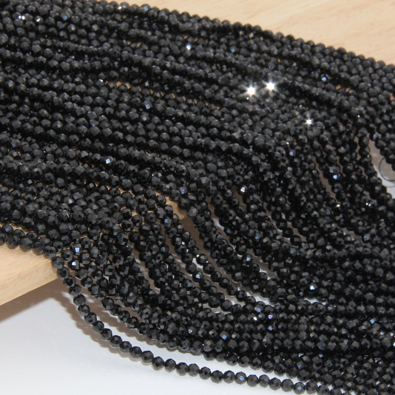 May include: A strand of black faceted gemstone beads. The beads are small and round, and they have a shiny, polished finish.