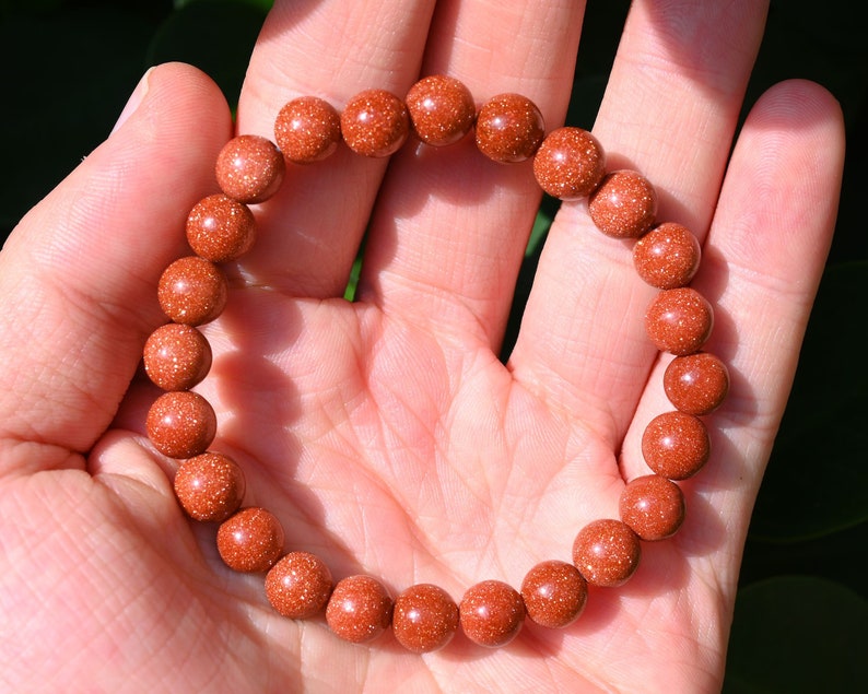 Puede incluir: Un brazalete de cuentas de color marr&oacute;n rojizo hecho de cuentas de piedra arenisca. El brazalete est&aacute; hecho de cuentas redondas con una textura moteada.