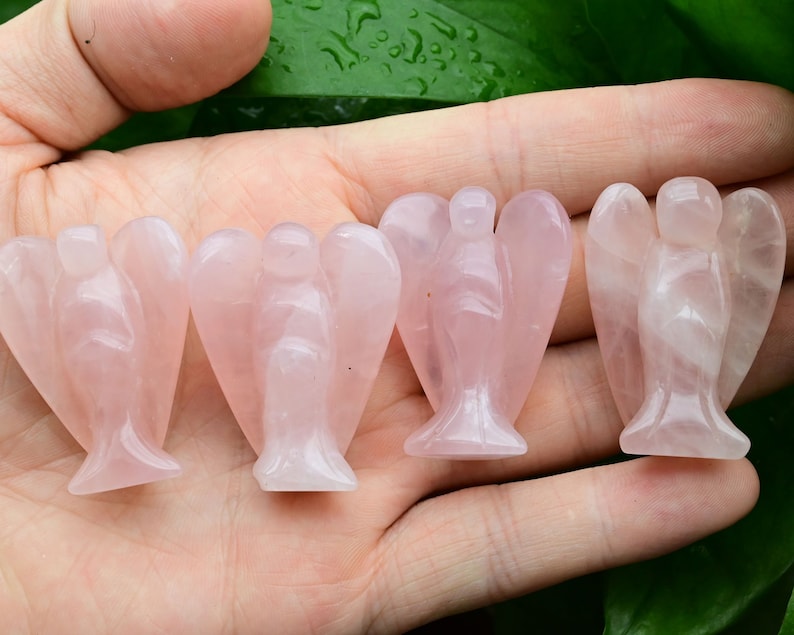 Puede incluir: Cuatro peque&ntilde;as figuras de &aacute;ngeles de cuarzo rosa. Cada &aacute;ngel tiene alas detalladas y una t&uacute;nica fluida. Los &aacute;ngeles se sostienen en una mano sobre un fondo de hojas verdes. El cuarzo rosa tiene una calidad transl&uacute;cida.
