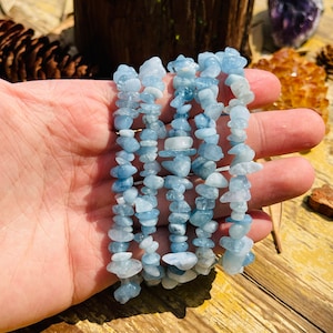 May include: Five strands of aquamarine chip bead bracelets, stacked on top of each other, in a hand.