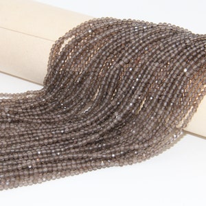 May include: A strand of smoky quartz beads, each bead is faceted and has a dark grey colour. The beads are arranged in a loose pile, showing the individual beads.