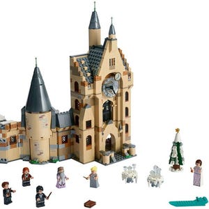 May include: A Lego set depicting a large tan and gray building with a clock tower, a smaller tower, and several miniature figures. Additional elements include a Christmas tree, tables, and a green sled.