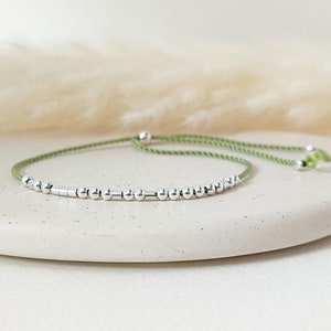 May include: A green string bracelet with silver beads. The bracelet is adjustable and can be tied to fit any wrist.