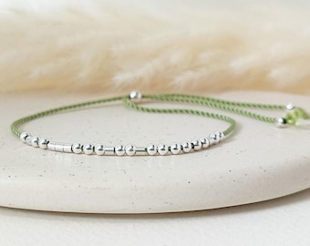 May include: A green string bracelet with silver beads. The bracelet is adjustable and can be tied to fit any wrist.