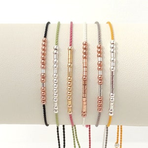 May include: A set of eight bracelets with different coloured cords and silver and gold beads. The bracelets are tied with a knot and have a tassel at the end.
