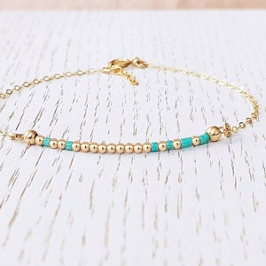 May include: A delicate gold chain bracelet with a row of tiny gold beads and turquoise beads.