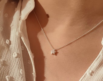 May include: A silver chain necklace with a small star pendant. The necklace is worn by a person with a white blouse.