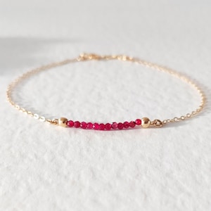 May include: A delicate gold chain bracelet with a single row of small, bright red ruby beads.