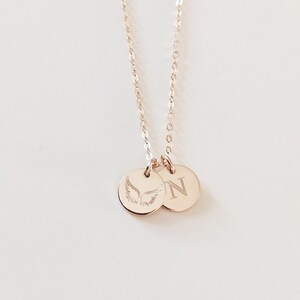 May include: A gold necklace with two charms. One charm has a pair of angel wings engraved on it, and the other charm has the letter "N" engraved on it.