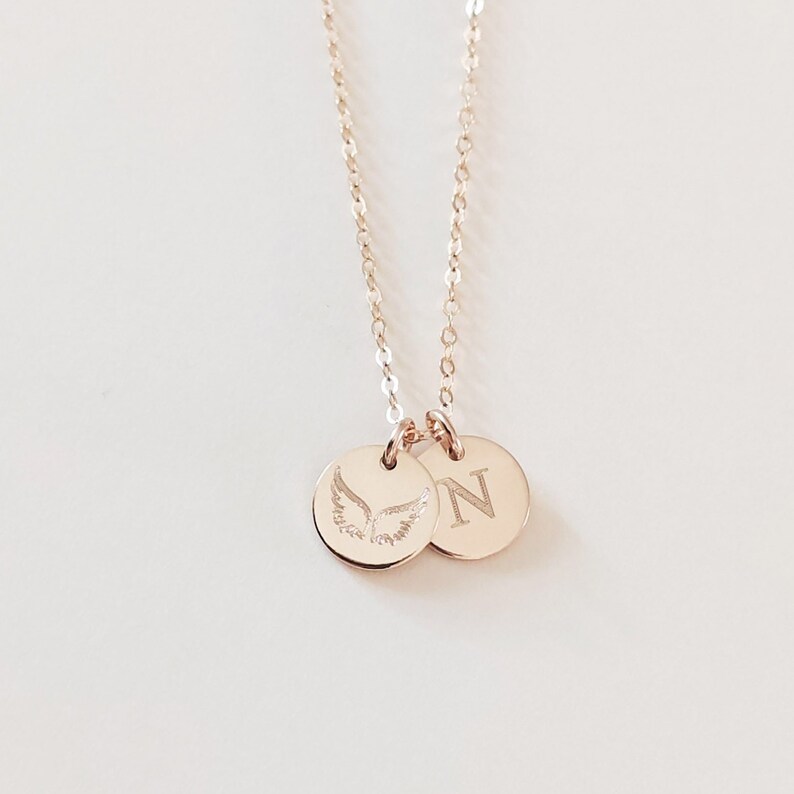 May include: A gold necklace with two charms. One charm has a pair of angel wings engraved on it, and the other charm has the letter "N" engraved on it.