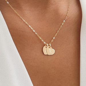 May include: A gold chain necklace with two heart-shaped pendants. Each pendant has a letter engraved on it, one with the letter "S" and the other with the letter "R".