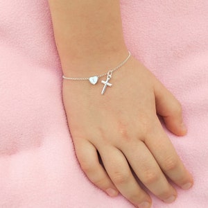 May include: A silver bracelet featuring a small cross charm and a heart charm engraved with the letter "E".