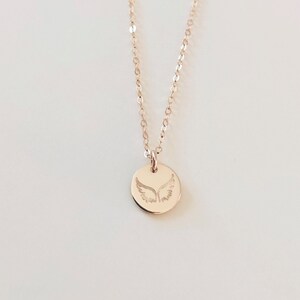 May include: A delicate gold necklace with a small round pendant featuring an engraved angel wing design.