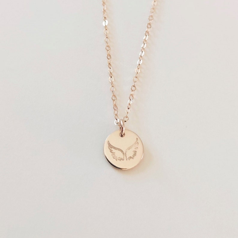 May include: A delicate gold necklace with a small round pendant featuring an engraved angel wing design.
