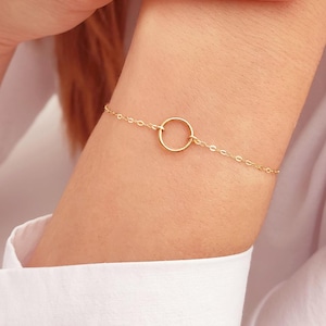 May include: A delicate gold chain bracelet with a simple circle pendant. The bracelet is made of a thin chain and the circle is about 1/2 inch in diameter.