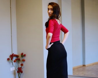 Könnte beinhalten: Eine Frau in einem roten Oberteil und einem schwarzen Rock posiert in einem Tanzstudio. Sie trägt nude-farbene Absätze und hat ihre Haare nach hinten gebunden.
