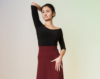 Könnte beinhalten: Eine Frau trägt ein schwarzes Langarmshirt und einen burgunderfarbenen Midirock. Sie steht mit der Hand auf der Hüfte und schaut zur Seite.
