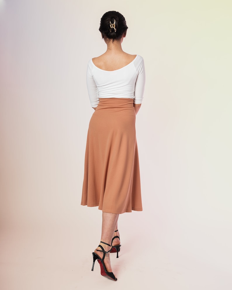K&ouml;nnte beinhalten: Eine Frau tr&auml;gt ein wei&szlig;es Langarm-Oberteil und einen braunen Midirock. Sie tr&auml;gt schwarze High Heels und hat ihre Haare nach hinten gebunden.