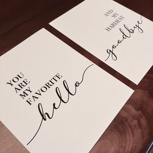 Puede incluir: Dos impresiones blancas con texto negro. La primera impresi&oacute;n dice "You are my favorite hello". La segunda impresi&oacute;n dice "And my hardest goodbye".