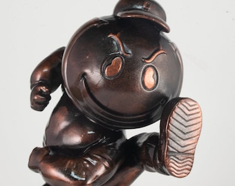 Könnte beinhalten: Eine bronzene Figur eines lächelnden Comic-Charakters, der eine Mütze trägt und mit einem erhobenen Bein rennt. Der Charakter hat einen großen, runden Kopf mit einem breiten Lächeln und einer einzigen hochgezogenen Augenbraue.