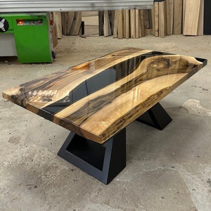 May include: A wooden coffee table with a black epoxy resin inlay. The table has a natural wood finish and black metal legs.