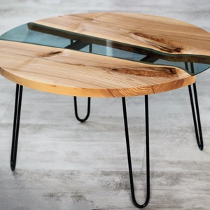May include: Round wooden coffee table with a clear resin river running through the center. The table has black hairpin legs.