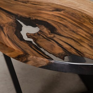 May include: Close-up of a wooden table top with a natural edge and a clear epoxy resin fill. The resin has a white and black swirl pattern. The table top is brown with dark brown streaks.