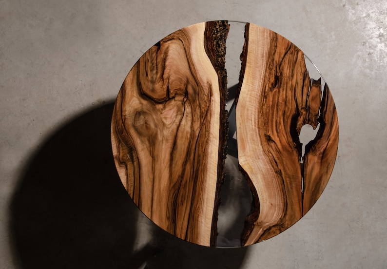 May include: A round wooden table top with a natural wood grain pattern and a clear epoxy resin fill. The table top is approximately 30 inches in diameter.