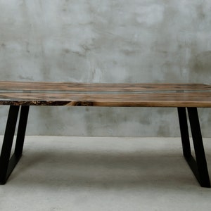 K&ouml;nnte beinhalten: Ein rechteckiger Holztisch mit nat&uuml;rlicher Holzmaserung und einer Einlage aus klarem Epoxidharz. Der Tisch wird von schwarzen Metallbeinen getragen. Der Tisch ist ca. 183 cm lang, 91 cm breit und 76 cm hoch.