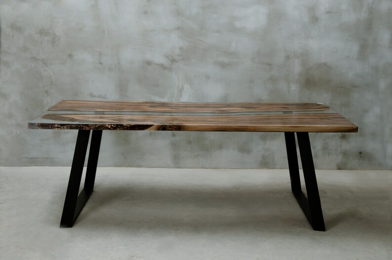 K&ouml;nnte beinhalten: Ein rechteckiger Holztisch mit nat&uuml;rlicher Holzmaserung und einer Einlage aus klarem Epoxidharz. Der Tisch wird von schwarzen Metallbeinen getragen. Der Tisch ist ca. 183 cm lang, 91 cm breit und 76 cm hoch.