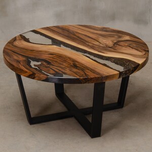 May include: Round wooden coffee table with a black metal base. The table top has a clear epoxy resin finish with a natural wood grain pattern.