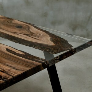 K&ouml;nnte beinhalten: Moderner Esstisch mit einem Design aus lebendem Holz. Der Tisch hat eine klare Harzeinlage und dunkle Beine. Die Holzmaserung ist von satten Braunt&ouml;nen, und das Harz ist transparent. Der Tisch ist etwa 183 cm lang.
