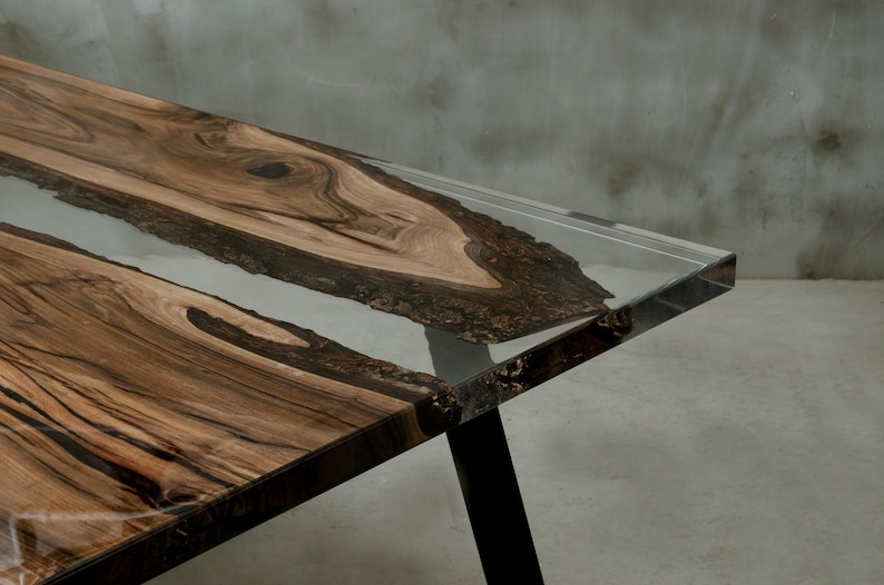 K&ouml;nnte beinhalten: Moderner Esstisch mit einem Design aus lebendem Holz. Der Tisch hat eine klare Harzeinlage und dunkle Beine. Die Holzmaserung ist von satten Braunt&ouml;nen, und das Harz ist transparent. Der Tisch ist etwa 183 cm lang.