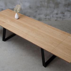 May include: A light wood dining table with a black metal frame. The table has a leaf that can be extended to make it longer.