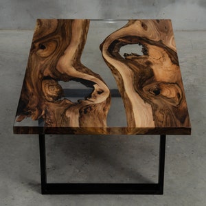 Op de afbeelding: Een rechthoekige salontafel met een tafelblad van levend hout en heldere epoxyhars die de natuurlijke knopen en scheuren vult. De tafel heeft een zwart metalen frame.