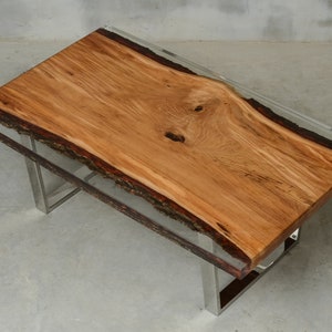 May include: A wooden table top with a live edge and clear epoxy resin. The table has a stainless steel base.