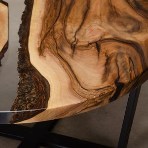 May include: A round wooden table top with a natural wood grain pattern and a clear epoxy resin inlay. The table top is supported by a black metal base.