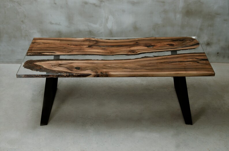 K&ouml;nnte beinhalten: Ein rechteckiger Couchtisch mit einer Tischplatte aus Holz mit lebendiger Kante und einem Inlay aus klarem Harz. Der Tisch hat schwarze Metallbeine. Das Holz hat ein nat&uuml;rliches Maserungsmuster mit Braun- und Beiget&ouml;nen. Der Tisch ist etwa 122 cm lang.