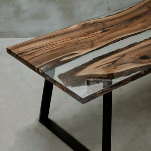 K&ouml;nnte beinhalten: Ein handgefertigter Holztisch mit einem Design mit lebendiger Kante. Die Tischplatte verf&uuml;gt &uuml;ber einen transparenten Epoxidharzfluss, der durch die Mitte verl&auml;uft. Der Tisch wird von schwarzen Metallbeinen getragen. Abmessungen: ca. 183 cm lang, 91 cm breit und 76 cm hoch.