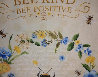 May include: A beige fabric with a gold inscription that reads "Bee Kind Bee Positive". The inscription is surrounded by a decorative gold border. The fabric is decorated with a bee, flowers, and a beehive.