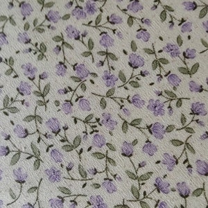 May include: A close-up of a fabric with a light beige background and a repeating pattern of small purple flowers and green leaves.