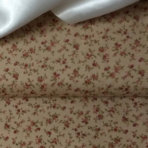 May include: A close-up of a beige fabric with a small, repeating floral pattern. The flowers are a light pink color and are scattered across the fabric.