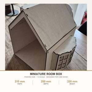 Può includere: Una scatola stanza in miniatura in legno chiaro con tetto a capanna e una finestra a bovindo con motivo a griglia. La struttura è etichettata come modello in scala 1:12 per legno da 3 mm, con 310 mm di larghezza, 250 mm di profondità e 320 mm di altezza.