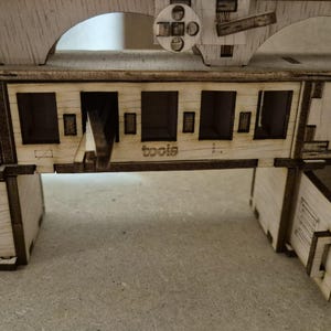 Op de afbeelding: Een lasergesneden houten miniatuurwerkbank met meerdere lades, een centraal compartiment met het woord tools en een klein kastdeurtje aan de rechterkant. De structuur heeft een lichte houtnerfafwerking met donkere, gebrande randen.