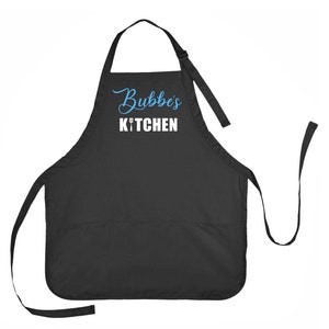 May include: Black apron with the text "Bubbe's KITCHEN" in blue and white. The apron has a bib, waist ties, and an adjustable neck strap. A fork and knife graphic is between the words "Bubbe's" and "KITCHEN".